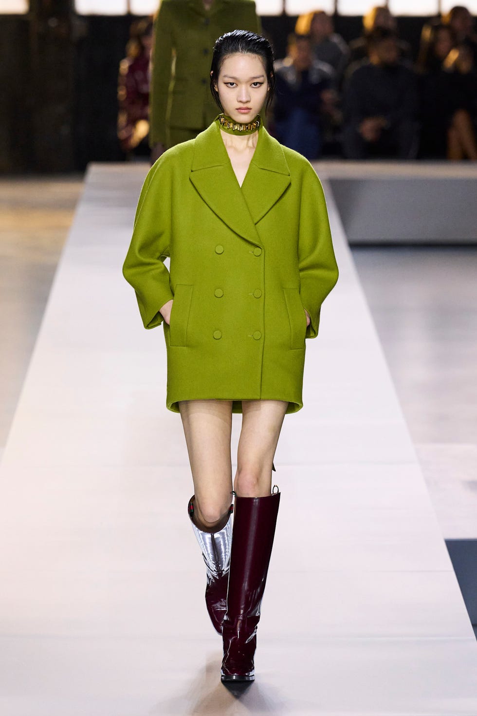 Fashion model walking the runway in a bright green oversized coat and unique boots