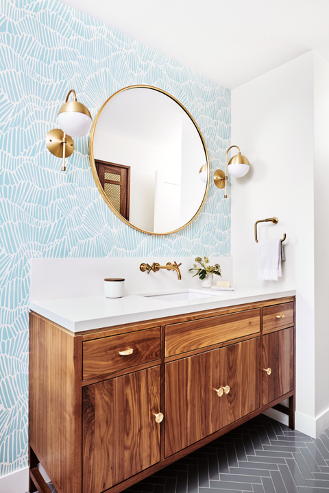 guest bathroom with light blue and white patterend shell wallpaper, brown cabinets, gold mirror