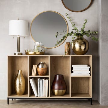 a wall decorating with wooden furniture, a circular mirror, a plant and lamp