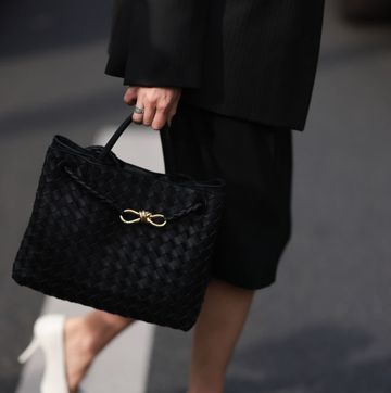 a woman carrying a black leather tote bag by bottega veneta with a black skirt and white pump while crossing the street in paris in a roundup of best laptop bags for women 2024