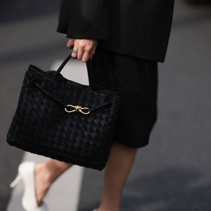 a woman carrying a black leather tote bag by bottega veneta with a black skirt and white pump while crossing the street in paris in a roundup of best laptop bags for women 2024
