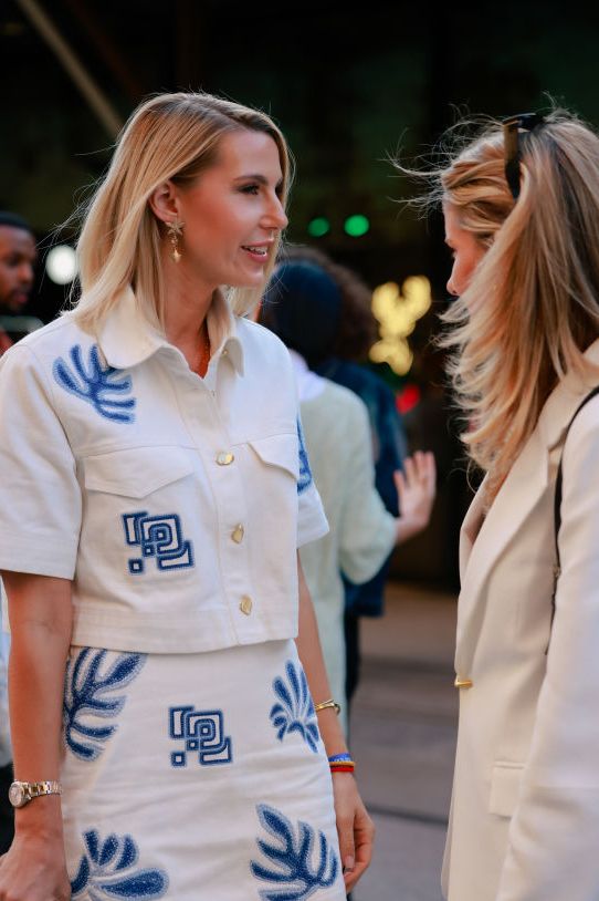 a woman wearing a white denim jacket with a blue embroidered print and matching mini skirt in a selection of the best travel outfits for women 2024