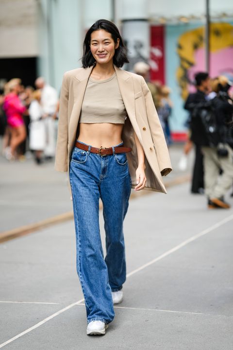 a woman wearing a tan crop top, blazer draped over her shoulders, baggy jeans, and sneakers during new york fashion week in a roundup of cute summer outfits 2023