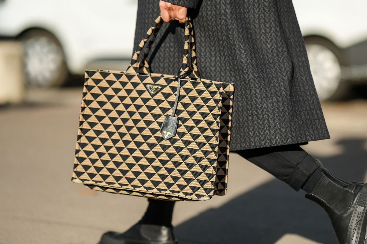 a guest at paris fashion week carries a prada tote bag to illustrate a guide to the best designer tote bags 2023