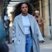 a guest at fashion week 2023 wears a white t shirt and jeans and a gray coat to illustrate a roundup of the best t shirts for women 2023