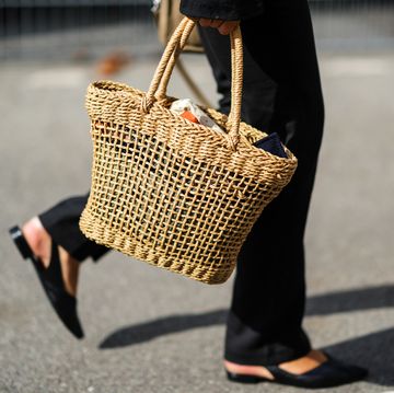 a woman at copenhagen fashion week walks with a straw bag to illustrate a story about the best straw bags of 2023