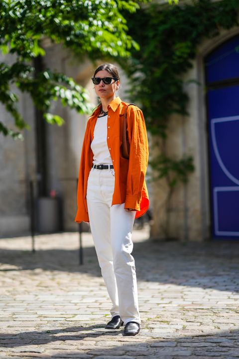 a woman wearing a white tee and jeans with an oversize orange button down during copenhagen fashion week in a roundup of cute summer outfits 2023