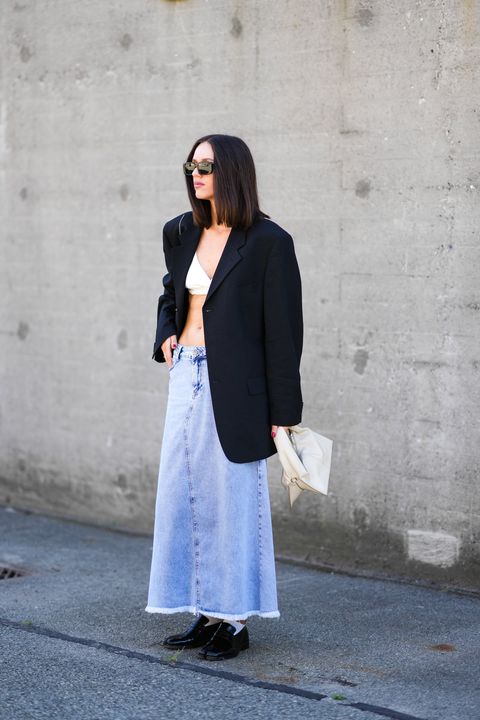 a woman wearing a denim maxi skirt with a white bra top and oversize black blazer on the street during copenhagen fashion week in a roundup of cute summer outfits 2023