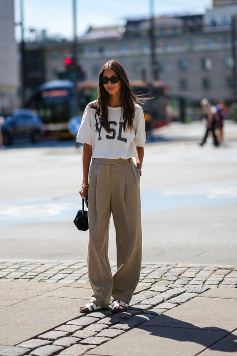 a woman wearing a a ysl t shirt, beige trousers, and flat sandals during copenhagen fashion week in a roundup of cute summer outfits 2023