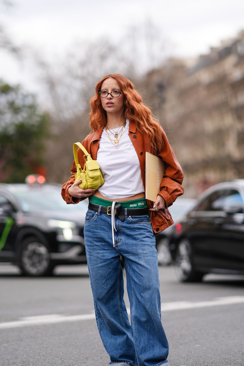 een jonge vrouw poseert in een wit t shirt bruine jas en wijde jeans tijdens paris fashion week