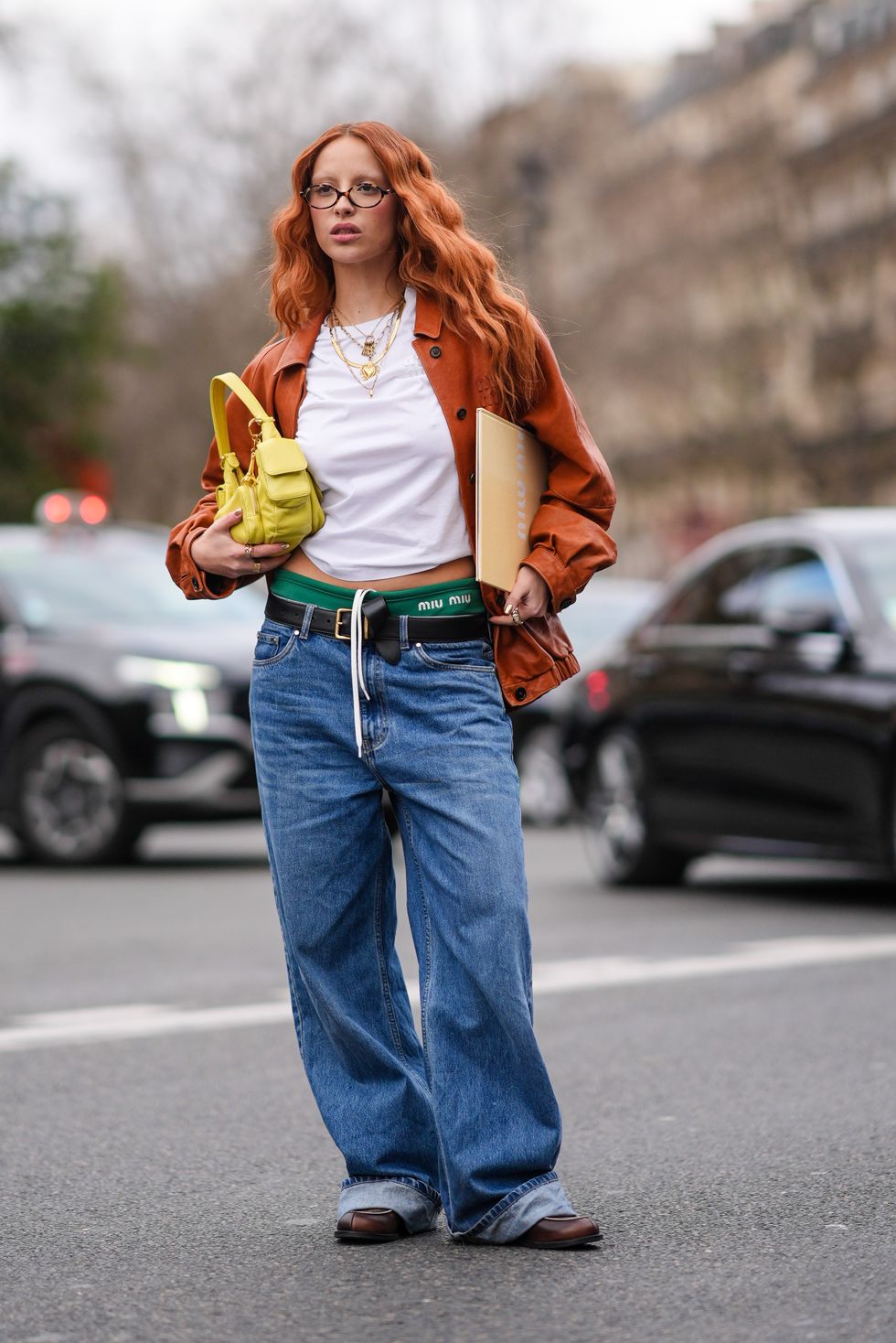 een jonge vrouw poseert in een wit t shirt bruine jas en wijde jeans tijdens paris fashion week