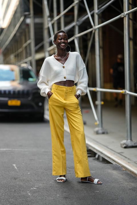 a woman wearing a cropped ivory sweater, yellow pants, and white flat sandals during new york fashion week in a roundup of cute summer outfits 2023