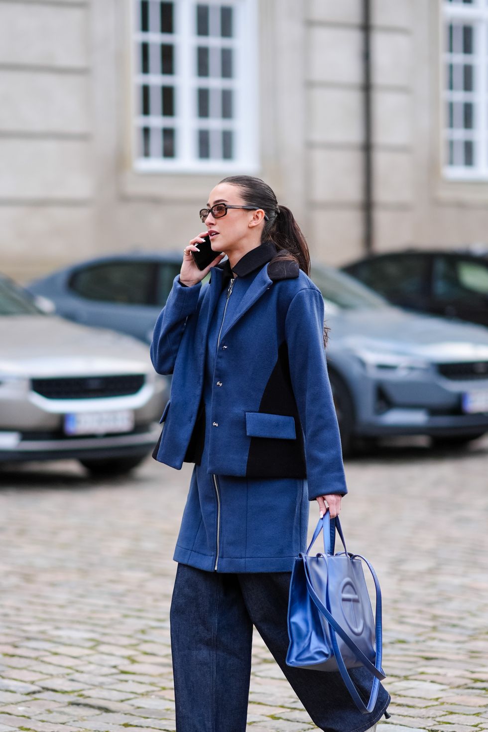 een gast draagt donkerblauwe jas, wijde jeans en schoenen met een spitse neus tijdens paris fashion week