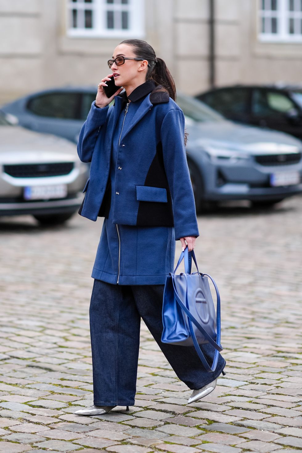 een gast draagt donkerblauwe jas, wijde jeans en schoenen met een spitse neus tijdens paris fashion week