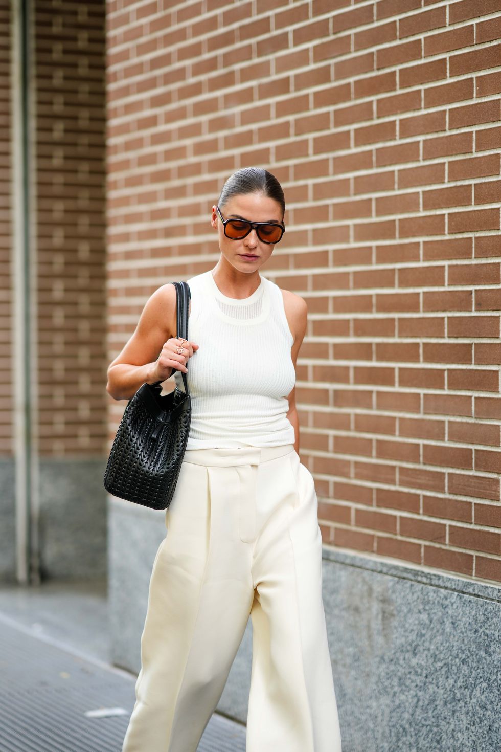 a woman wearing a white blouse, cream pants, black bag and aviator sunglasses on the street in a list of the best travel outfits for women in 2024