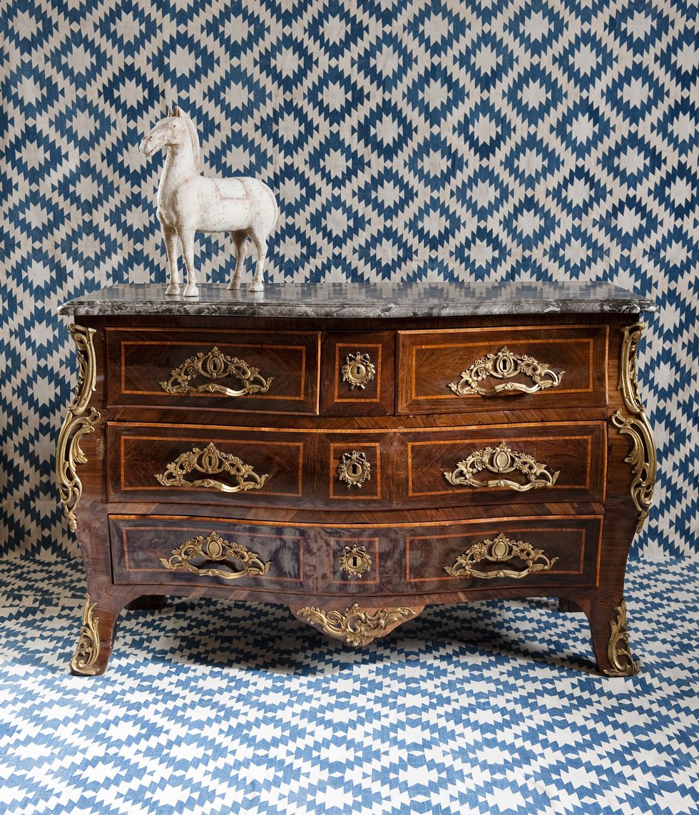 antique looking wood chest with a statue of a white horse on it against a background of blue and white geometrical wallpaper and flooring