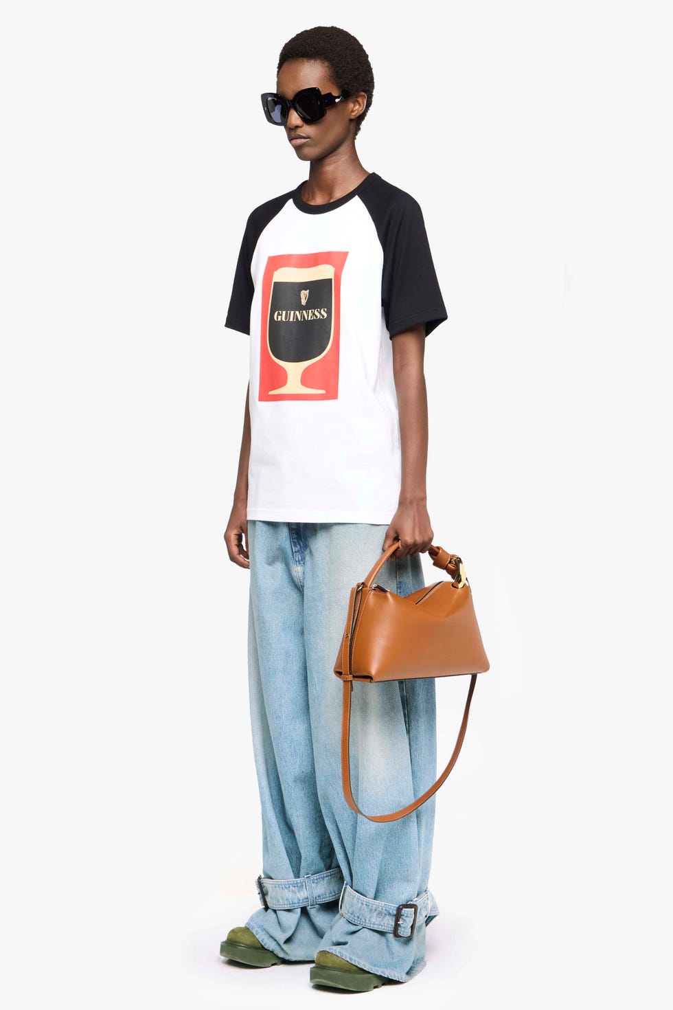 model wearing a guinness themed tshirt and loose jeans holding a brown handbag