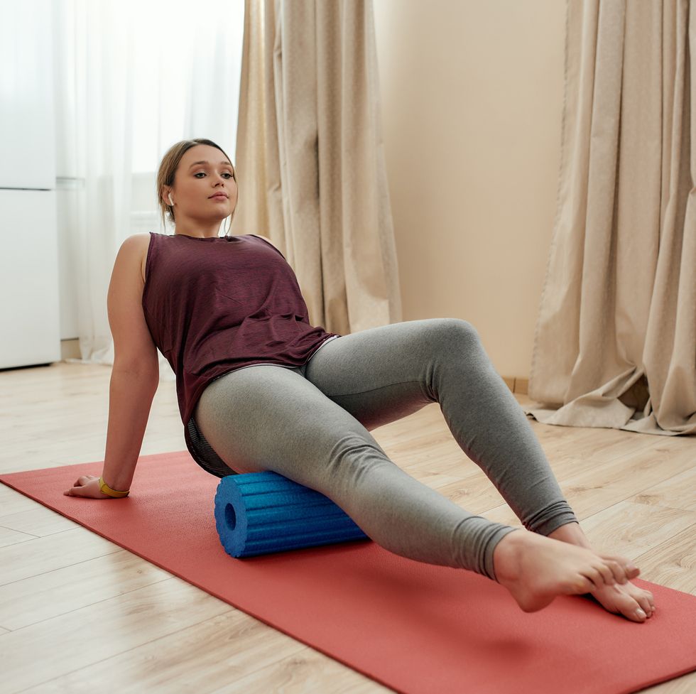 gym at home full length shot of young curvy woman in sportswear exercising using foam roller on a yoga mat at home