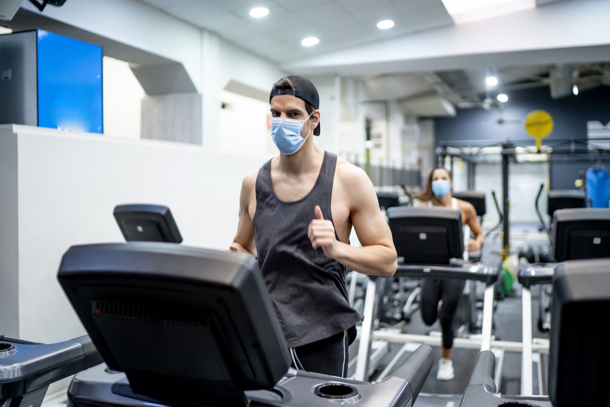 several young people running on treadmill in gym wearing face mask
