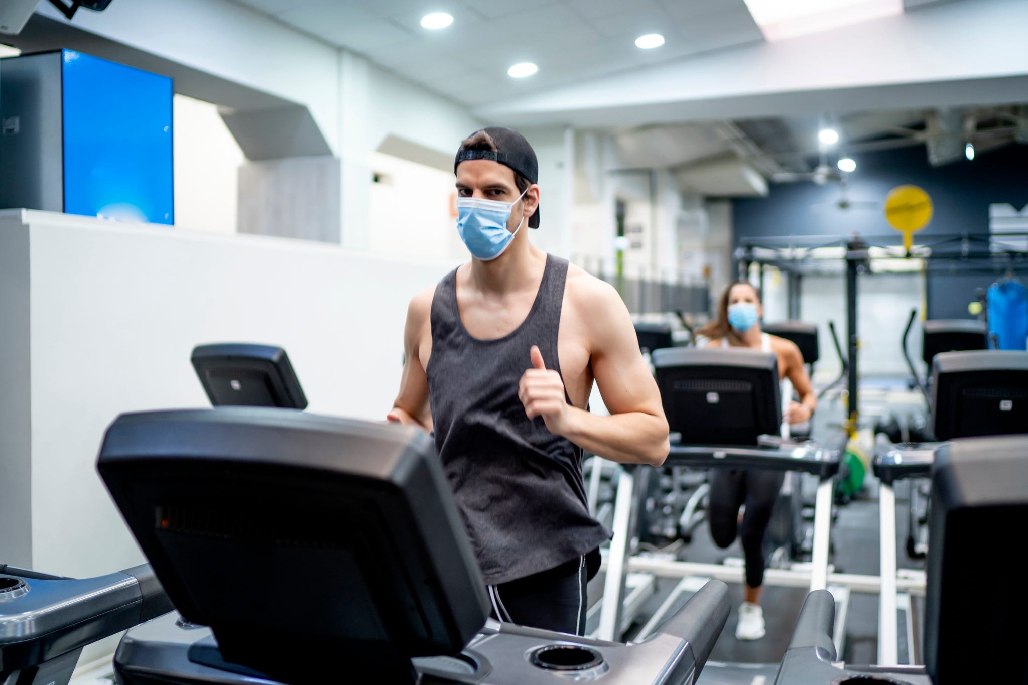 several young people running on treadmill in gym wearing face mask