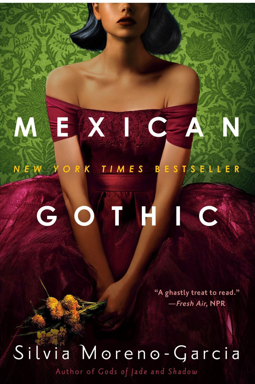 mexican gothic by silvia moreno garcia book cover featuring a woman in a wine red dress holding yellow flowers sitting in front of a green patterned wallpaper that features flowers