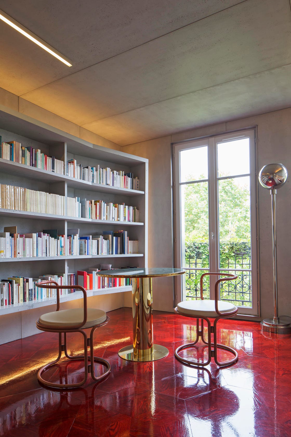 paris apartment with shiny red floor bookshelf and brass table with two chairs