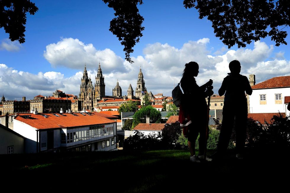 Nadat ze de Camino de Santiago hebben afgelegd staan twee mensen op een heuvel die uitzicht biedt op de Kathedraal van Santiago de Compostela in de Spaanse regio Galici