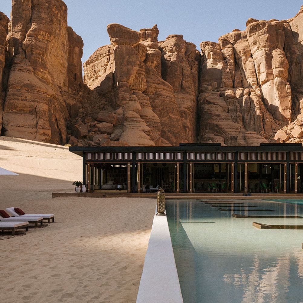 a pool with chairs and umbrellas by a building with large rocks