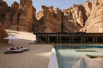 a pool with chairs and umbrellas by a building with large rocks