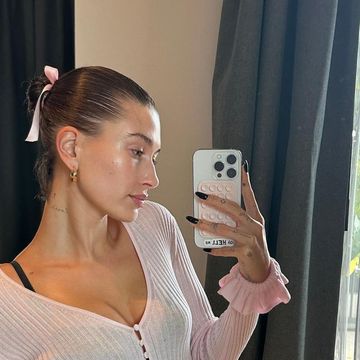 hailey bieber taking a mirror selfie wearing a pink cardigan and ribbon in her hair
