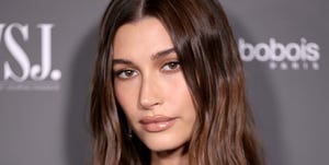 hailey bieber with long dark brown hair worn down poses on a red carpet wearing black