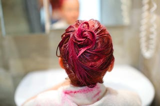 an elementary school age girl dyes her hair pink with a white towel over her shoulders in a gray bathroom near the sink and mirror back view, focus on hair