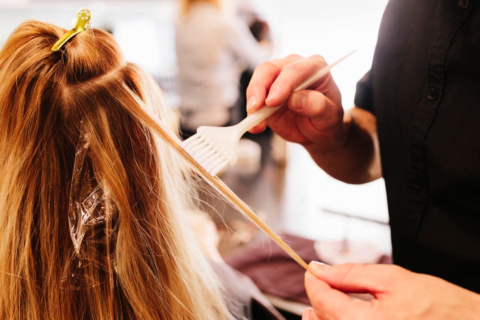 a hair colourist, a man using a paintbrush to cover sections of a womans blonde hair