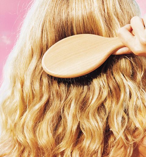 woman holding hair brush brushing her blonde hair
