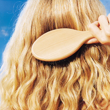 person brushing long curly blonde hair in the sun