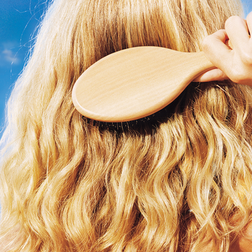 person brushing long curly blonde hair in the sun