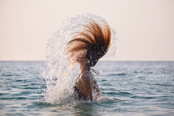 asian woman doing a water spin with her hair in the ocean during sunset 