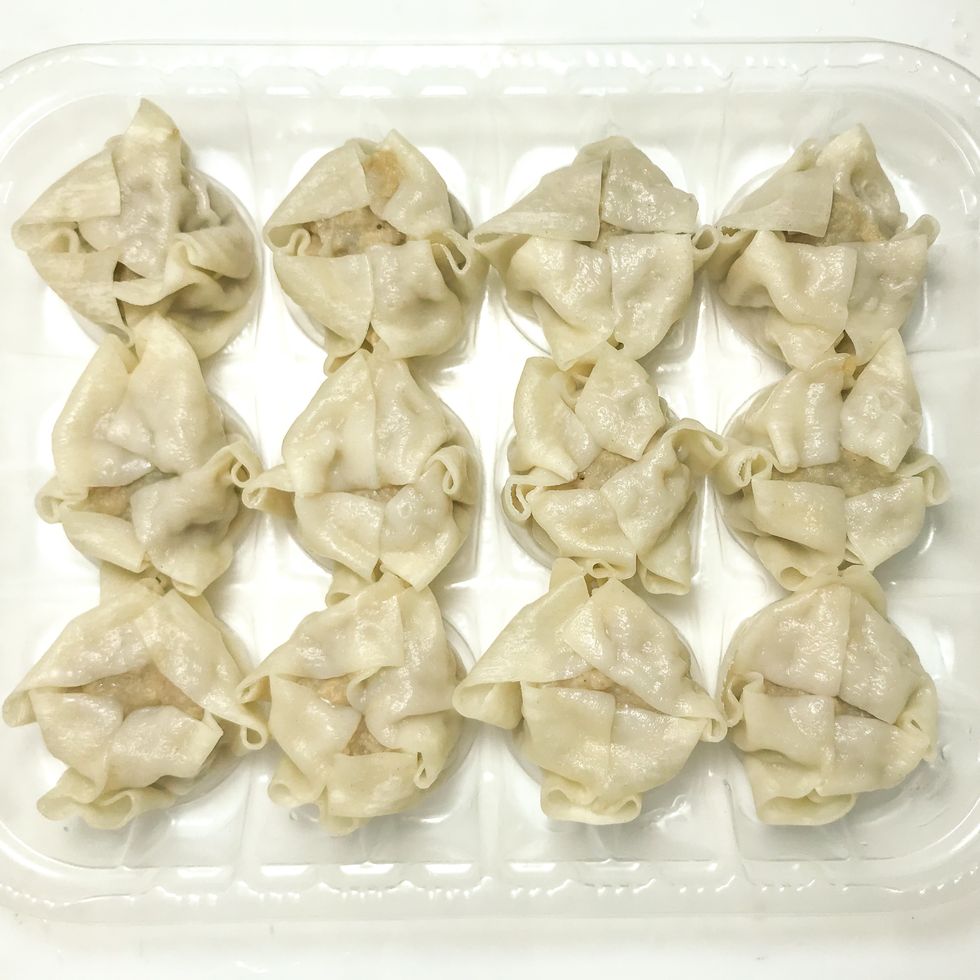 half cooked dozen shumai in transparent disposable plastic tray on white background