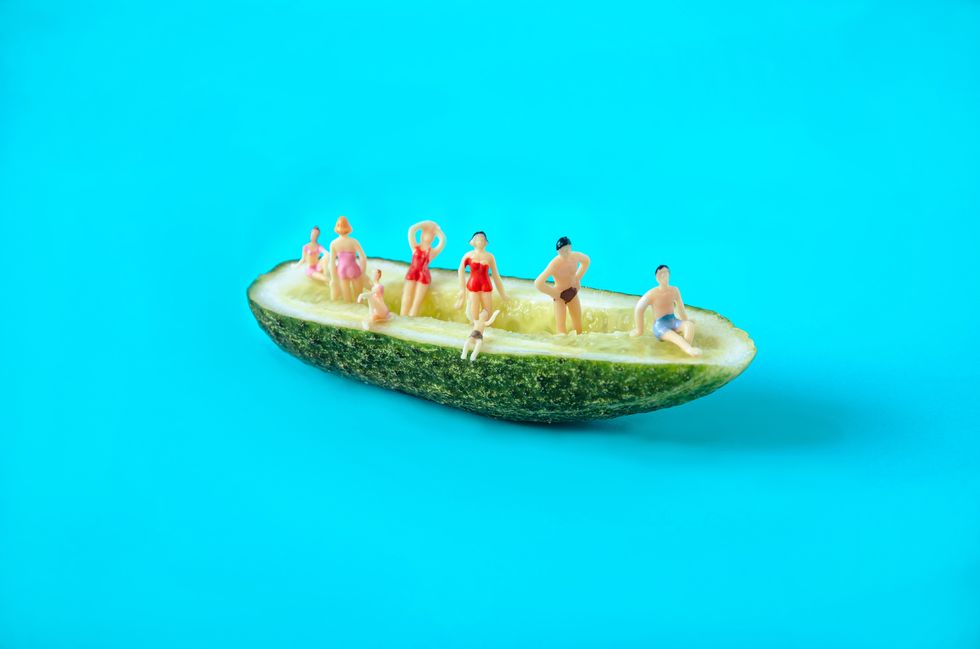 Medio pepino con mini personas contra el diseño de fondo azul pastel diseño surrealista para vacaciones de ocio de verano por el concepto creativo mínimo de mar para la agencia de viajes banner o editorial