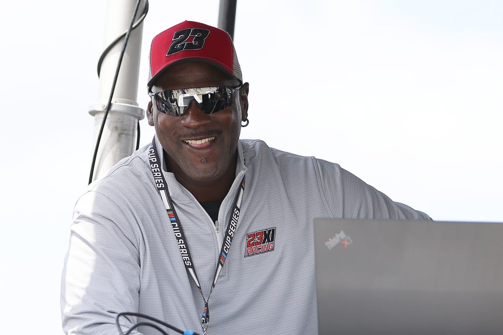 michael jordan smiling on a pit box while wearing a 23 hat