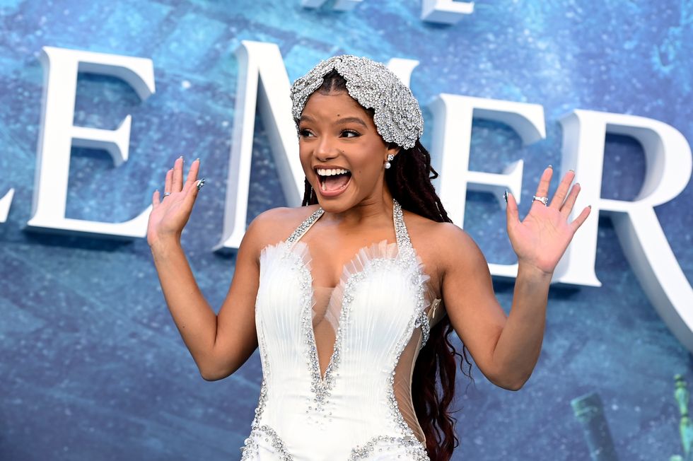 halle bailey smiling and waving with both hands at a film premiere