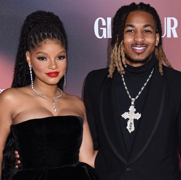 halle bailey and ddg, a young couple stand looking at the camera and smile, she wears a short black dress and he wears a black suit
