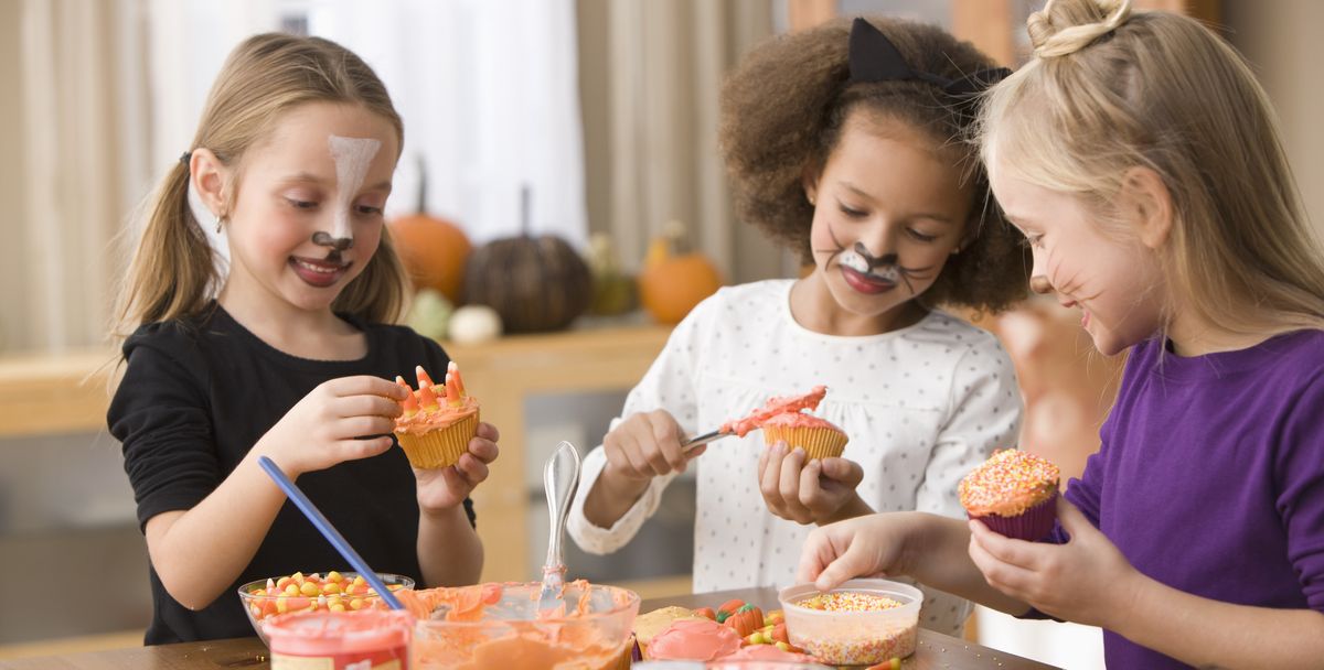 girls in halloween costumes decorating cupcakes