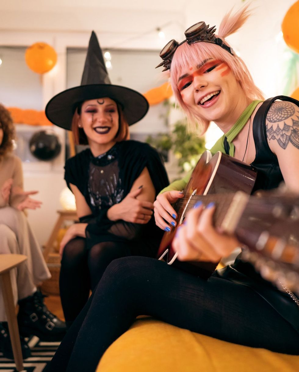 three young women in costumes enjoying fun at halloween party activities, singing, playing guitar