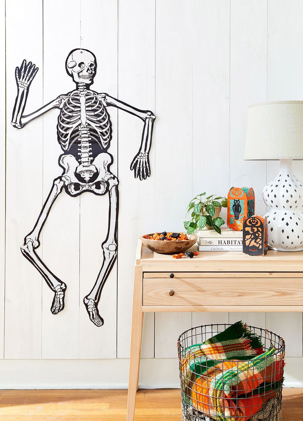 room decorated with paper skeleton on wall, bowl of candy, and paper lanterns for halloween party
