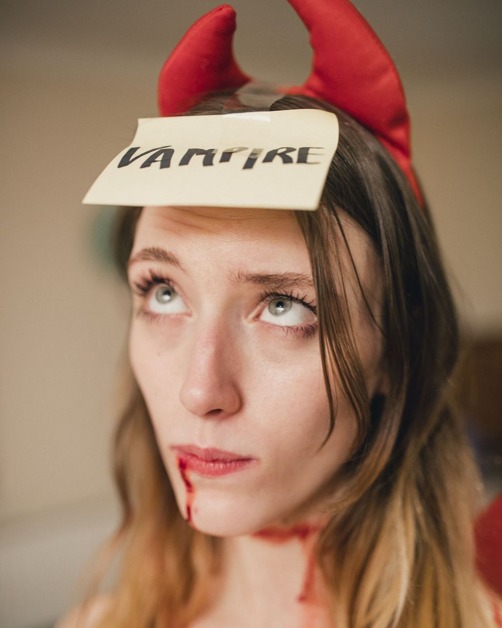 woman in devil costume with card on her forehead that says vampire, a halloween version of the name game party activity