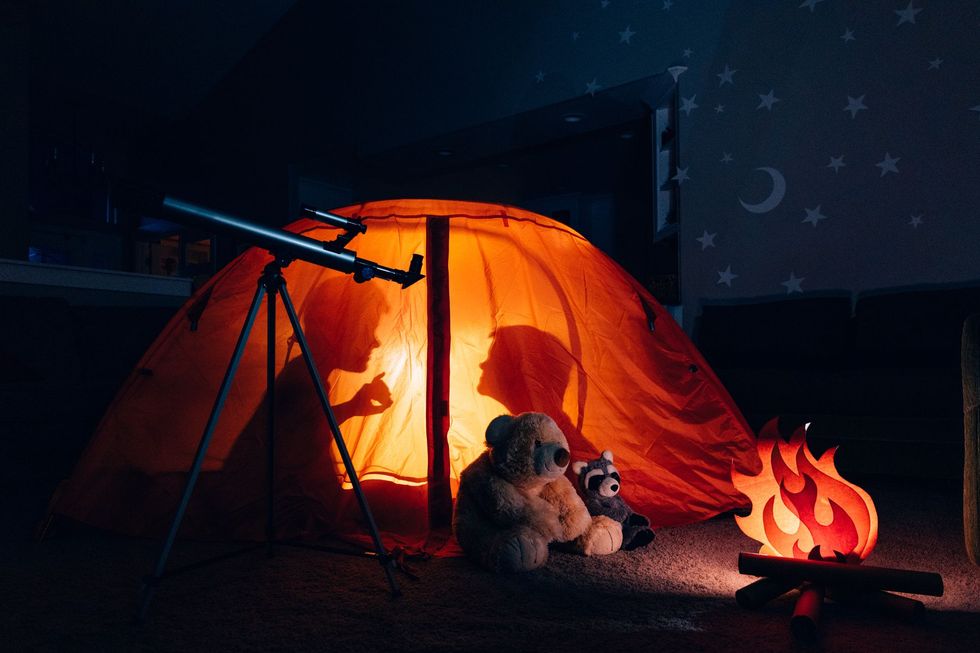 silhouette of two boys in tent camping indoors telling ghost stories for a halloween activity