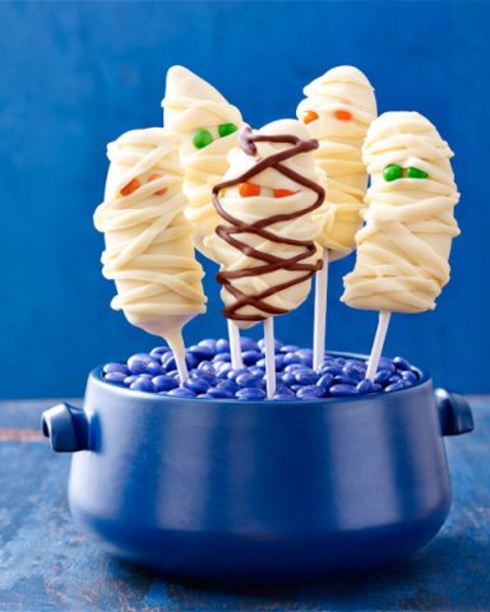 banana mummies  on sticks the sticks are set in a little blue pot filled with blue m n ms