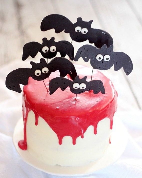 white frosted cake garnished with with red dripping ganache and vampire bat decorations