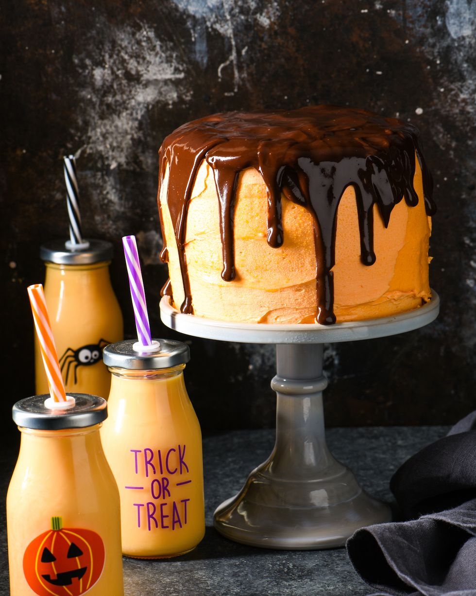 orange cream cake with chocolate ganache on cake stand with orange drinks